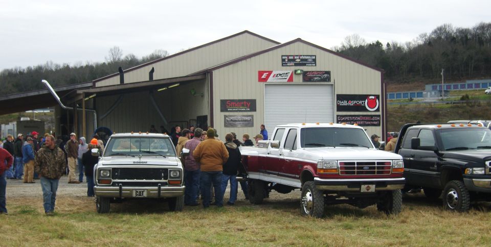 Three pickup trucks parked in front of a building with people gathered around