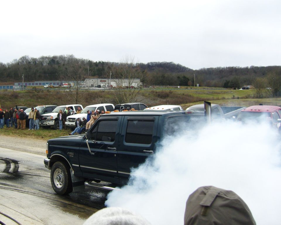 Dark blue pickup truck with a tall exhaust pipe, seen from the side, emitting a large cloud of white smoke