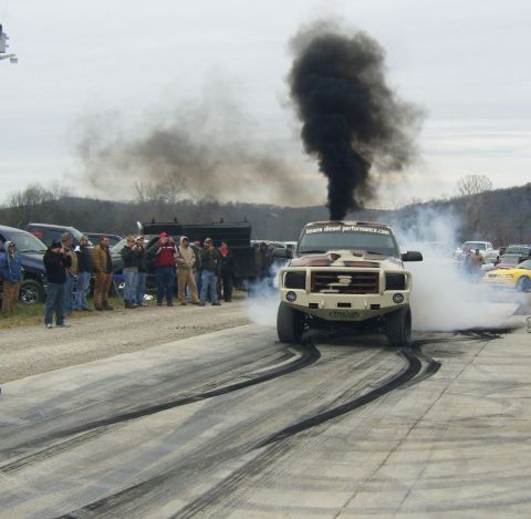 2007 Ford Mustang - A truck is shown performing a burnout, creating a large cloud of black smoke and leaving tire marks on the pavement.