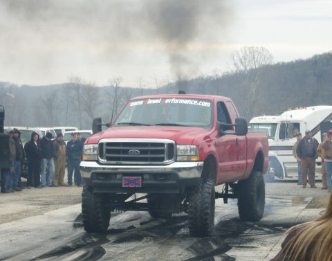 2007 Ford Mustang - A red Ford truck with a lifted suspension emits a large cloud of black smoke during an event.