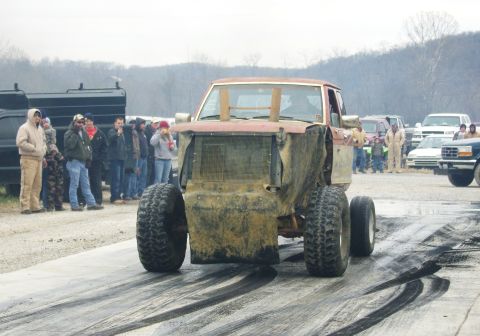 2007 Ford Mustang - A heavily modified truck with oversized tires sits on a drag strip, surrounded by spectators.