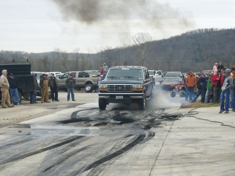 2007 Ford Mustang - A Ford F-Series truck performs a burnout, leaving tire marks on the asphalt as onlookers observe.
