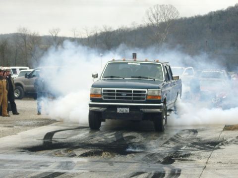 2007 Ford Mustang - A Ford F-Series truck performs a burnout, creating a large cloud of smoke on a paved track.