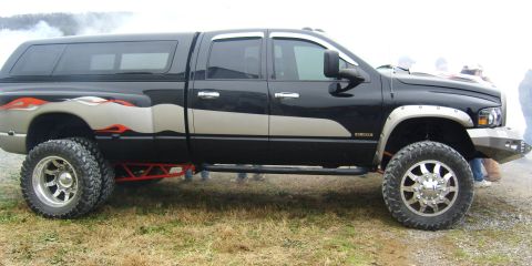2007 Ford Mustang - This lifted black pickup truck features flame decals and a camper shell, modified for off-road use.