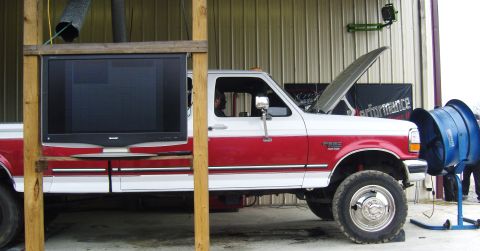 2007 Ford Mustang - A red and white pickup truck is set up for a dyno test with a large screen TV and a fan.
