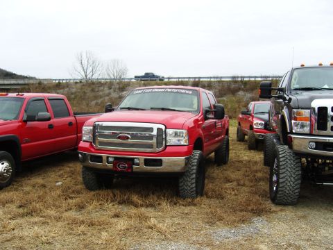 2007 Ford Mustang - Several lifted pickup trucks are parked together outdoors on a cloudy day.