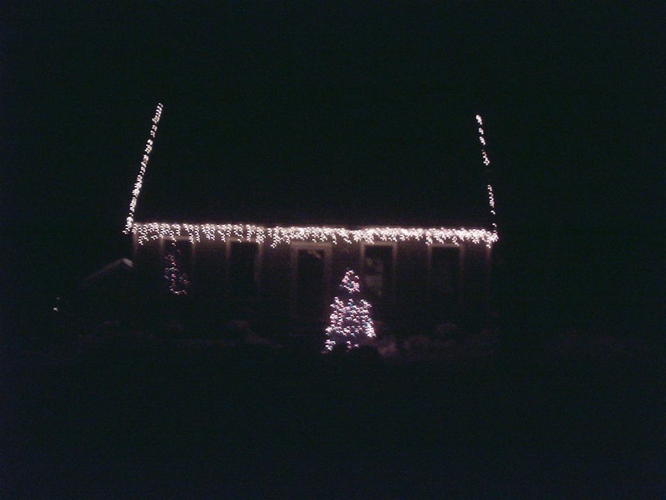House decorated with icicle lights and a Christmas tree, at night