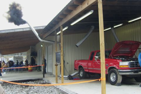 2007 Ford Mustang - Red Ford F-Series truck undergoing testing on a dynamometer, producing significant exhaust smoke.