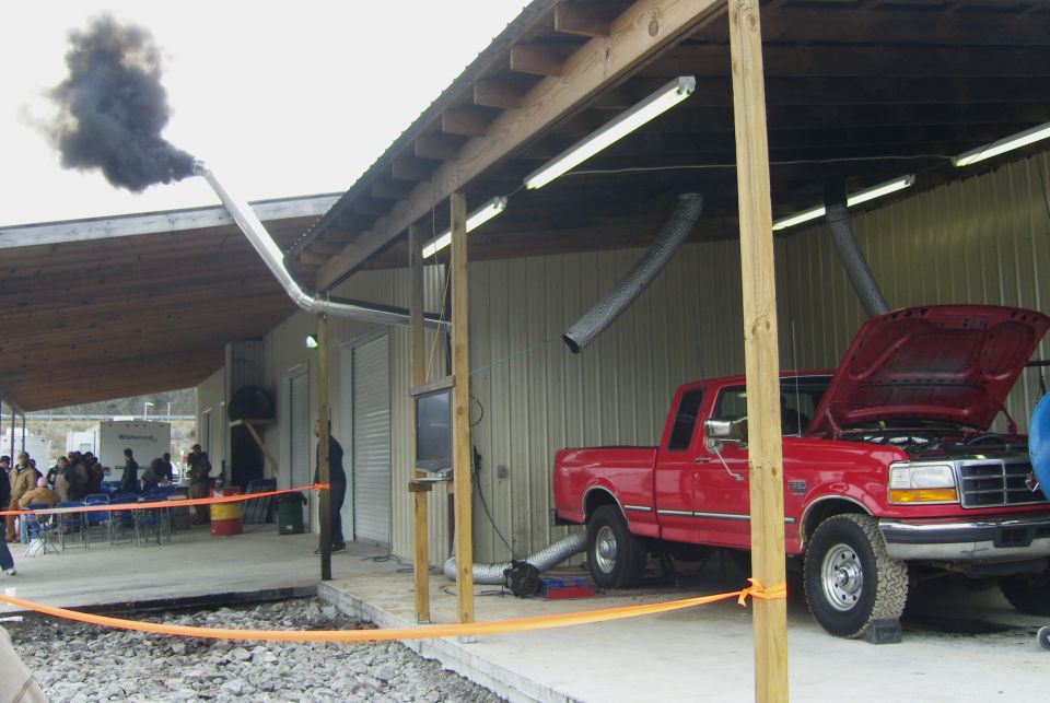 Red Ford F-Series pickup truck on a dynamometer, hood open, emitting black exhaust smoke