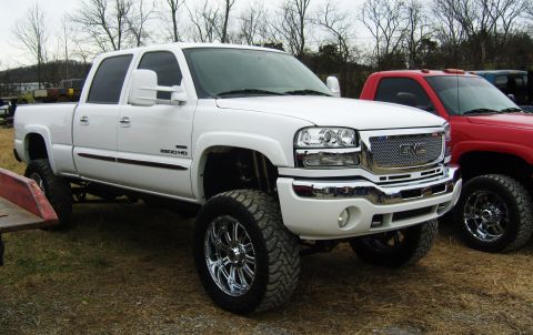 2007 Ford Mustang - A lifted white GMC Sierra pickup truck is parked next to a red truck under a cloudy sky.