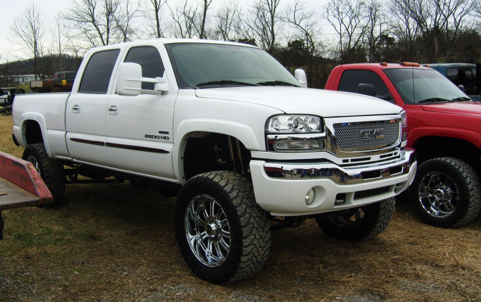White GMC Sierra 2500 HD pickup truck with chrome grille and rims, lifted suspension, parked outdoors