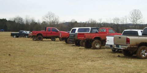 2007 Ford Mustang - A collection of muddy, lifted pickup trucks are parked in a field under an overcast sky.