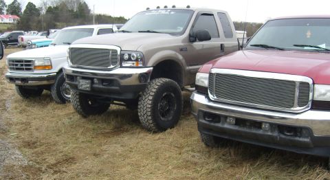 2007 Ford Mustang - Several pickup trucks are parked in a lot, with the middle truck being a lifted tan model.