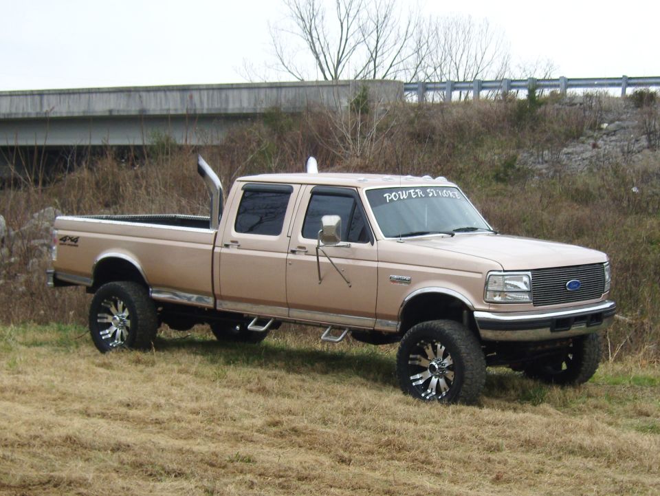 Tan Ford F-250 Super Duty pickup truck, 3q-front view, with dual exhaust stacks and custom wheels
