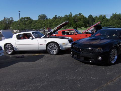 1977 Pontiac Trans Am - Three Pontiac Trans Am models are parked together, two with hoods open, under a clear blue sky.