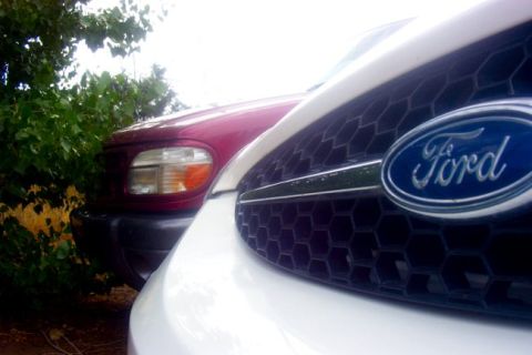 2000 Ford Taurus - A white Ford Taurus is parked next to a red SUV, with the Ford emblem clearly visible on the grille.