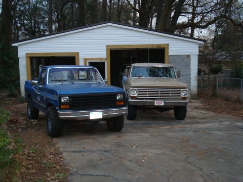 1985 Ford F-150 - Two pickup trucks, a blue Ford F-150 and a tan truck, are parked in front of a detached garage.