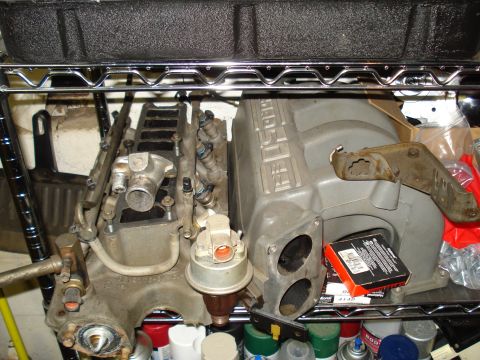 1991 Ford Bronco - Engine parts, including an intake manifold, are stored on a metal shelf.