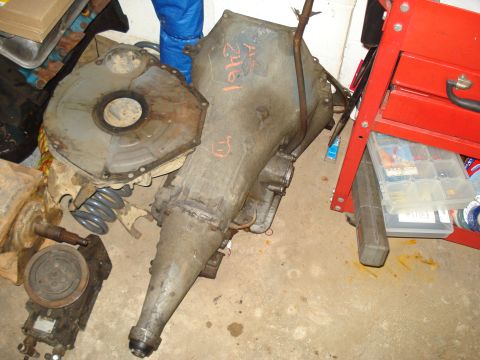 1991 Ford Bronco - Various automotive parts, including a transmission, are stored on a concrete floor next to a red tool cart.