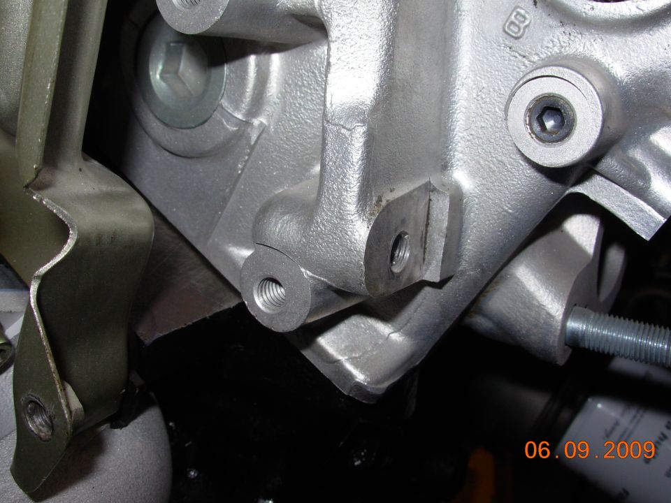 Close-up of a silver engine component with bolt holes and a threaded insert