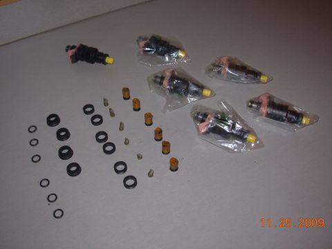 1991 Ford Taurus - Several fuel injectors and assorted O-rings are displayed on a flat surface.