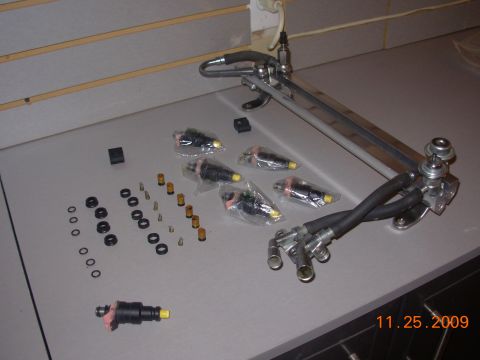 1991 Ford Taurus - A collection of fuel injectors and a fuel rail assembly are displayed, along with various small parts and seals.