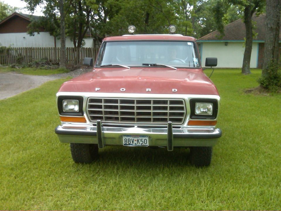 Red late-70s Ford truck front view on grass with chrome grille, Texas plate and roof-mounted round lights