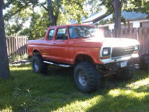 1978 Ford Bronco - This lifted pickup truck features a crew cab and is parked in a grassy yard with a fence in the background.