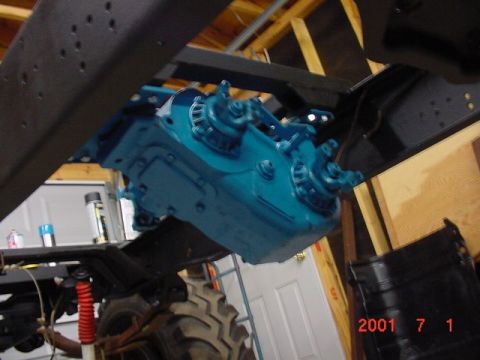 1978 Ford Bronco - Close-up of a blue transfer case assembly, part of a vehicle's drivetrain, with a tire and suspension visible.