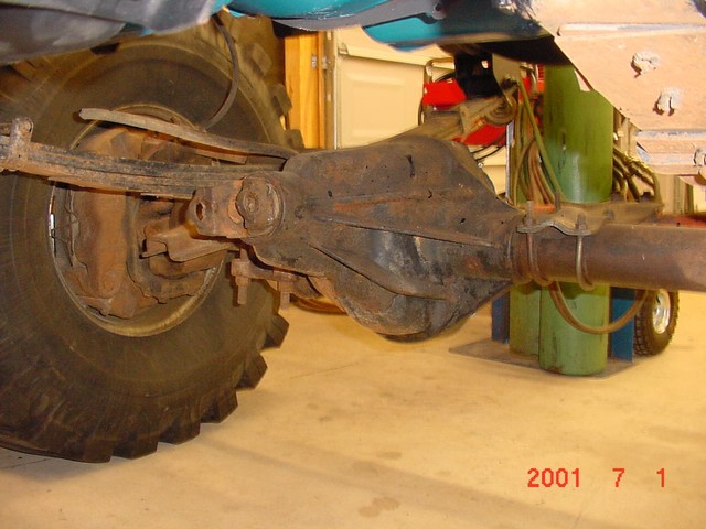 Rusty front solid axle and differential with drum brake and off-road tire underneath a vehicle