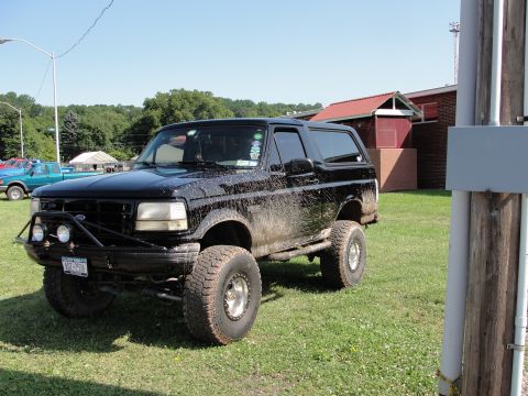 1995 Ford Bronco - This lifted black Ford Bronco is covered in mud, suggesting recent off-road use.