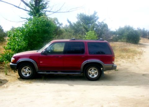 2000 Ford Taurus - Side view of a red Ford Explorer parked outdoors on a dirt road.