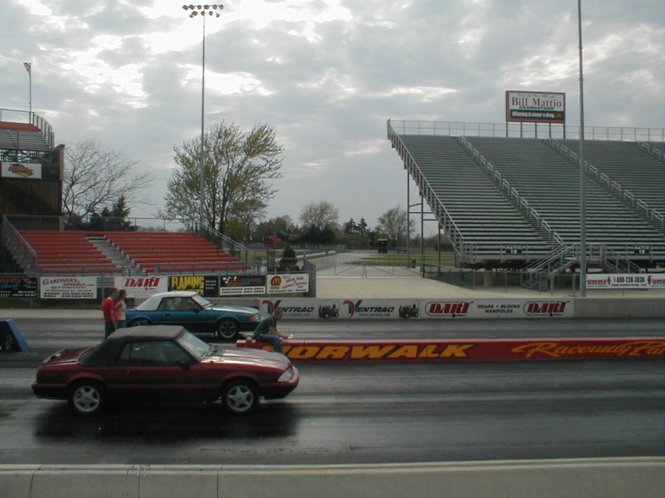 Red convertible Mustang from the early 1990s on a drag strip, with a blue convertible behind it
