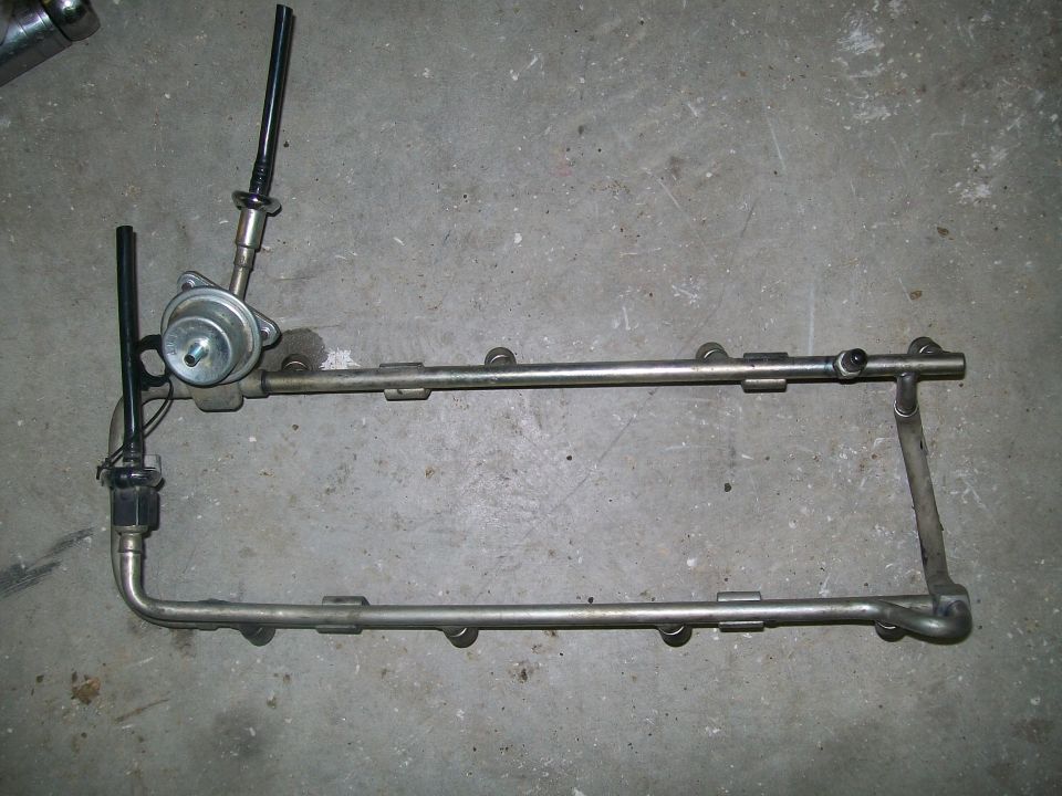 Two fuel rails with injector ports and stand pipes on a concrete floor