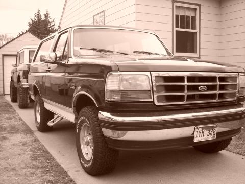 1992 Ford Bronco - Two Ford Broncos parked in a driveway, one in the foreground and another behind it.