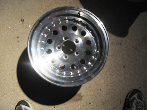 1986 Ford Bronco - A single aluminum wheel with a polished finish is shown lying on a concrete surface.