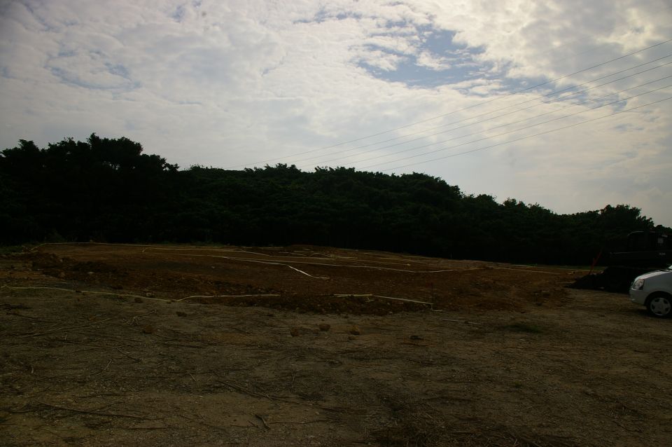 Silver car parked on dirt lot near trees, cloudy sky