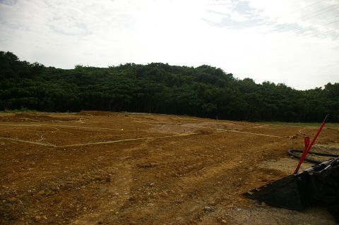 1986 Ford Bronco - A construction site is shown with marked plots in the dirt, a dense treeline in the background, and a bucket loader on the right.