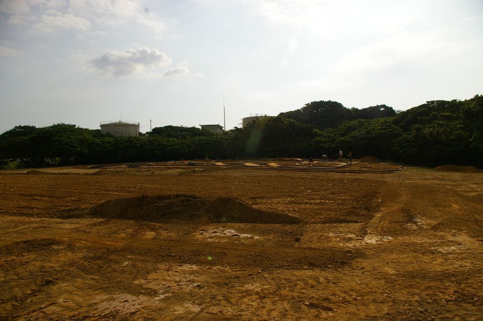 dirt field with some mounds of earth, trees and buildings in background