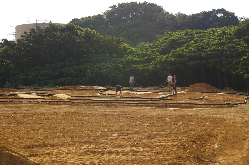 Dirt track with black tubing borders and piles of sand, with four people working