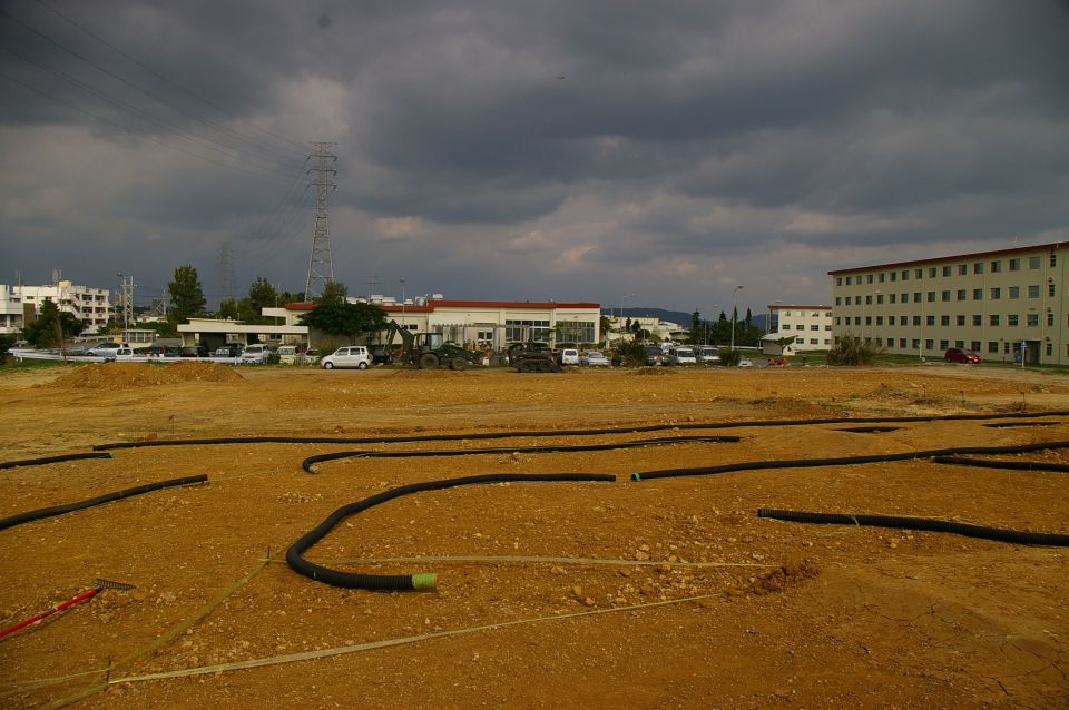 Construction site with black pipes laid out on dirt ground, buildings and power lines in background
