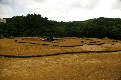 1986 Ford Bronco - An outdoor RC car track is laid out with black tubing defining the course, surrounded by dirt and vegetation.