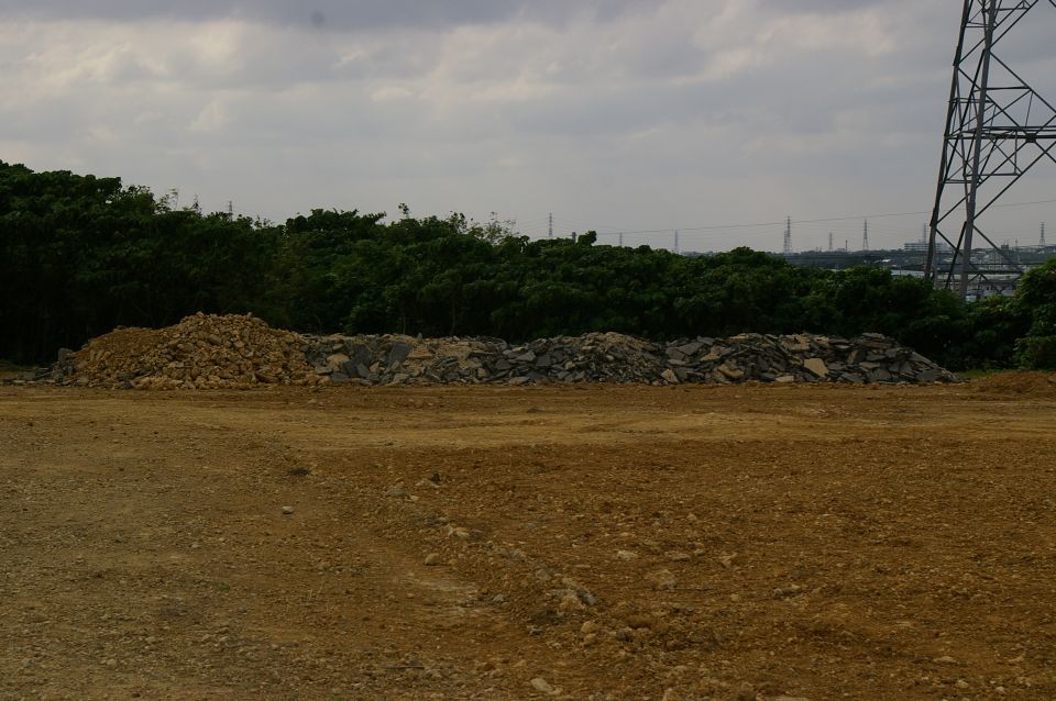 Construction site with piles of rubble and a large power line tower against a cloudy sky