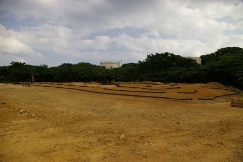 1986 Ford Bronco - Outdoor RC car track scene with a person and distant industrial structures.