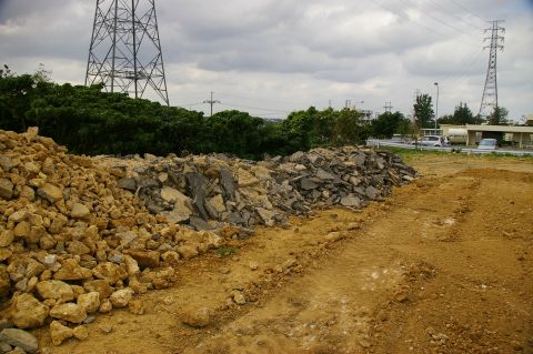 1986 Ford Bronco - A construction site scene features piles of rubble in the foreground with two vehicles visible on a road in the background.