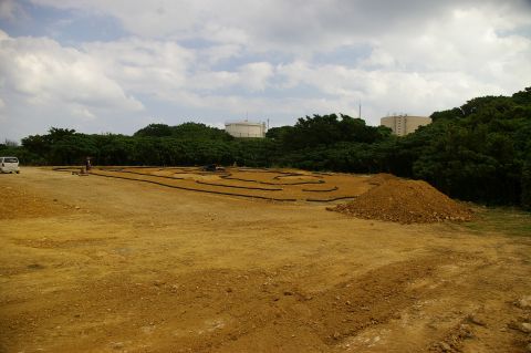 1986 Ford Bronco - A new RC car track is being built on a dirt lot, with trees and industrial tanks visible in the distance.