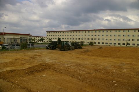 1986 Ford Bronco - A construction site with multiple buildings and various vehicles, including heavy machinery and a military truck, under a cloudy sky.