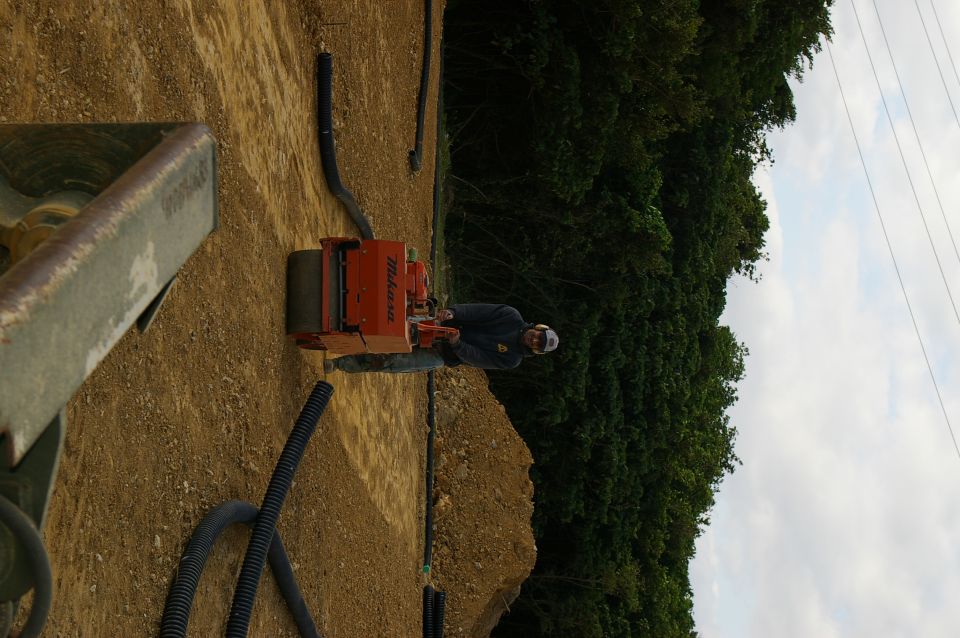 person operating a Mikasa compactor on a dirt construction site with trees in background