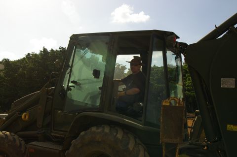 1986 Ford Bronco - A man operates a green backhoe loader under a partly cloudy sky.