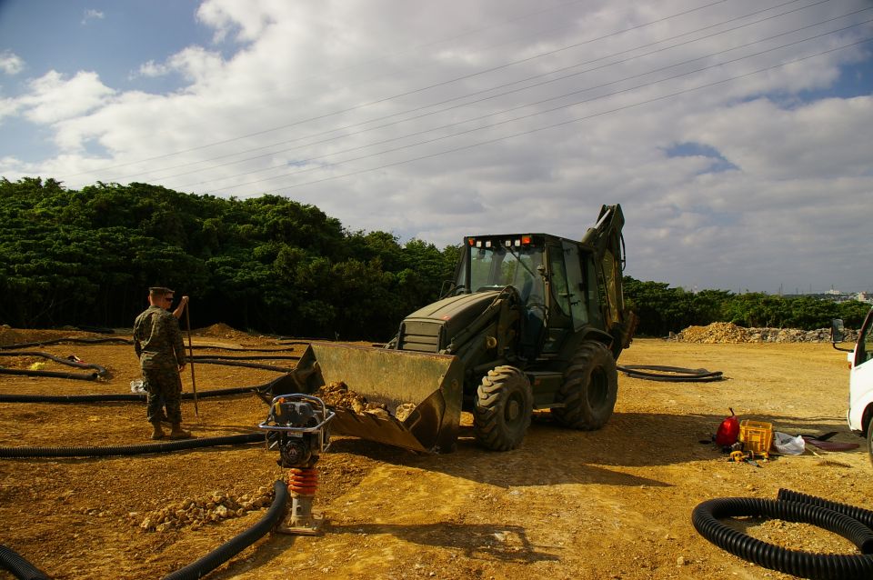 Backhoe loader with bucket raised, in a construction site with a person standing nearby